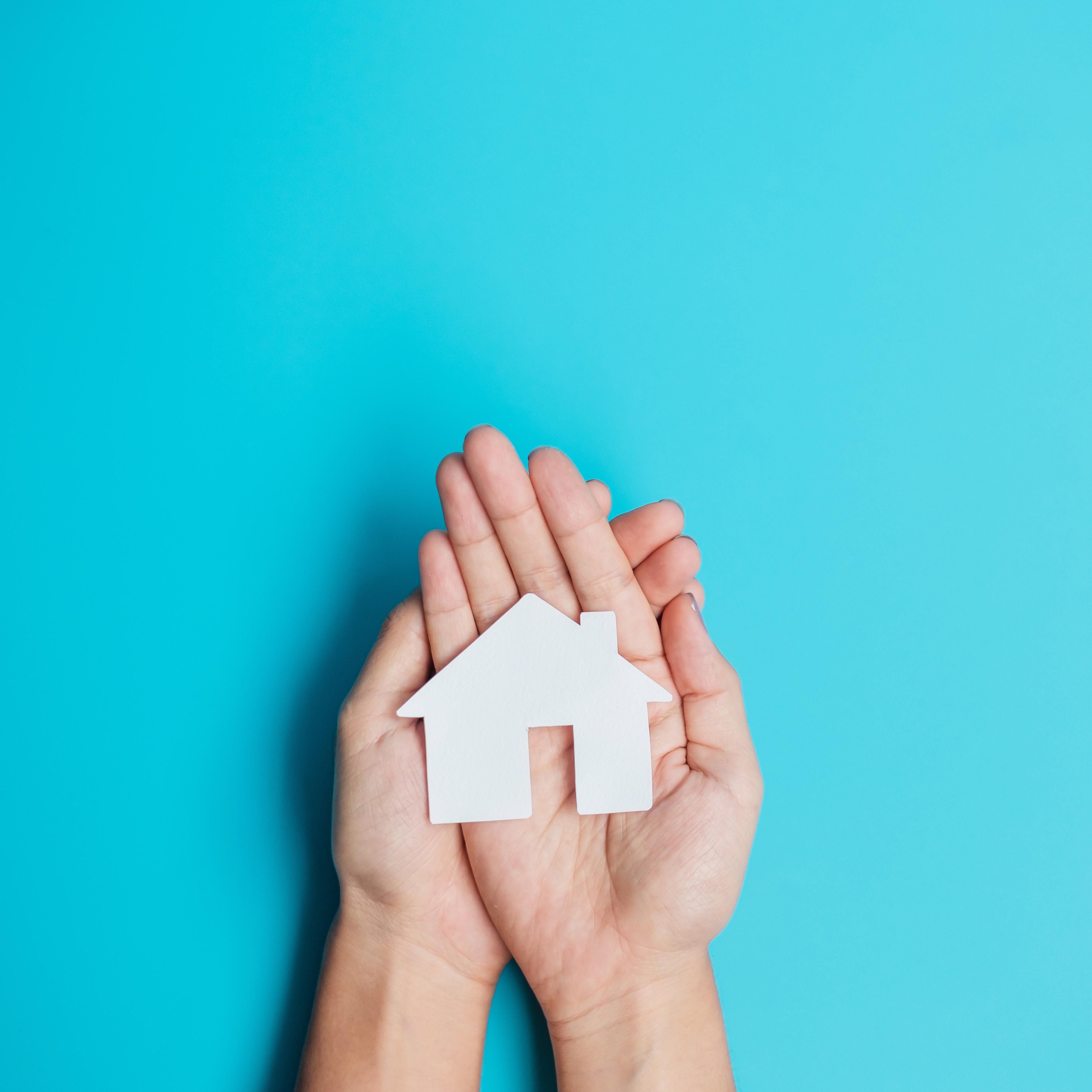 Hands holding a symbol of a house on a blue background