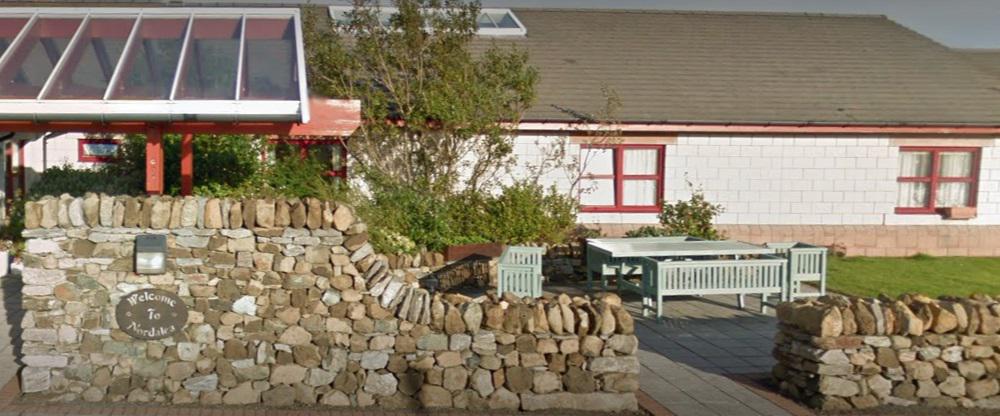 Front of single story building with a stone wall showing a sign saying welcome to Nordalea